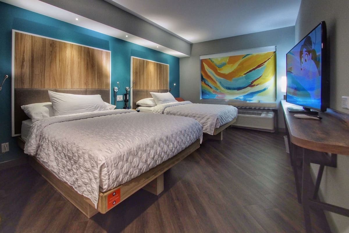 Quarto de hotel moderno com duas camas, uma televisão e um grande quadro abstrato na parede.