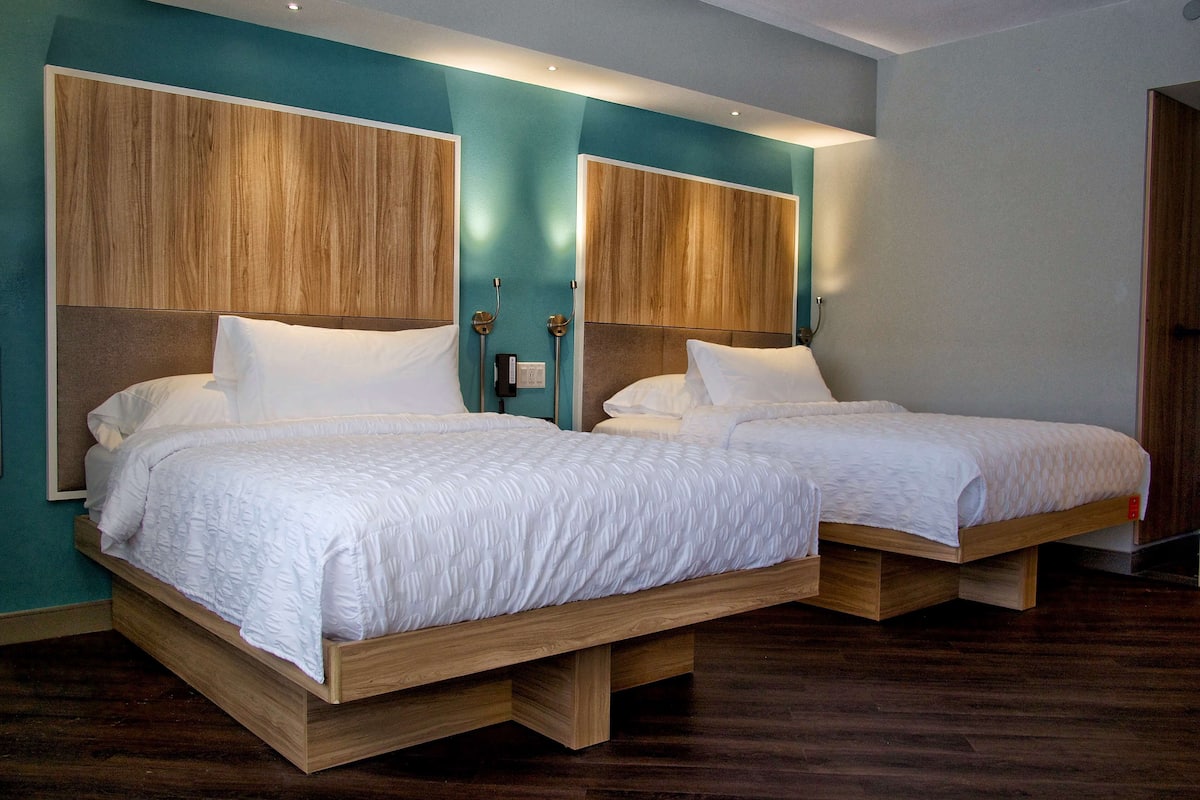 Quarto de hotel com duas camas de madeira, paredes verde-água e cabeceira de madeira.