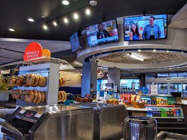 A food court with a doughnut machine, a beverage cooler, and a sign for bagels & donuts.