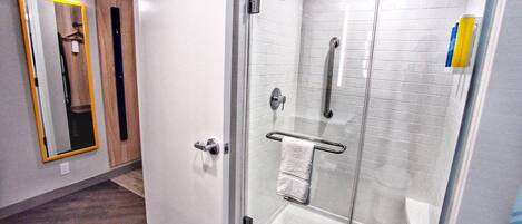 A modern bathroom with a glass shower enclosure, a white towel rack, and a mirror with a yellow frame.