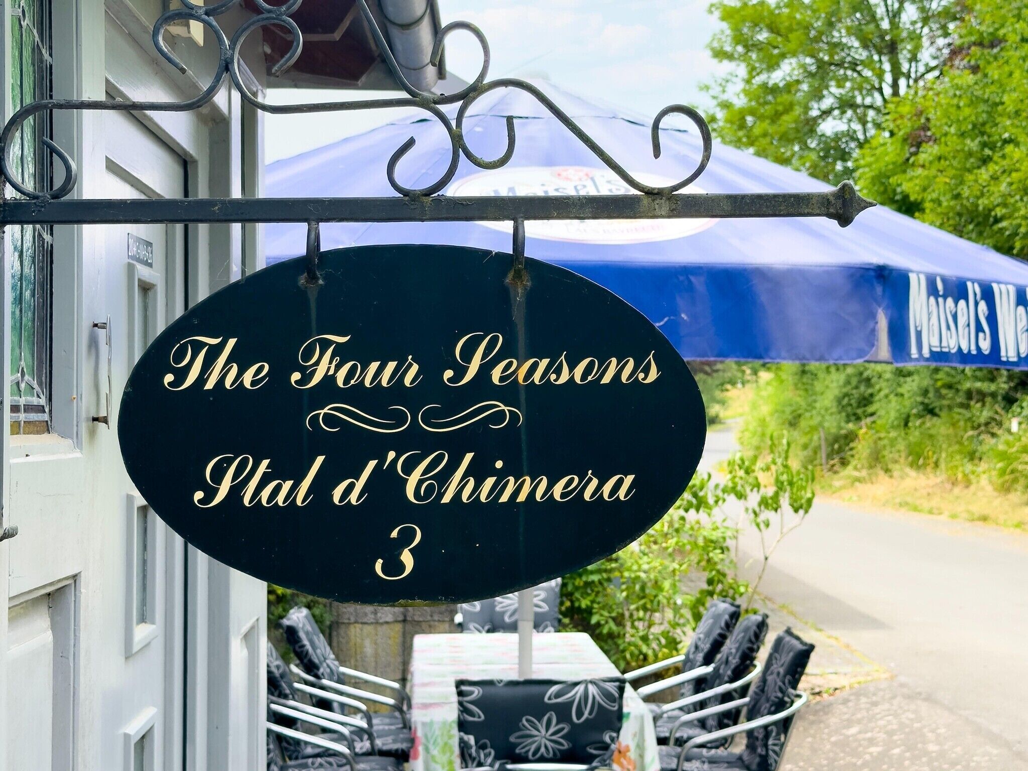A sign for 'The Four Seasons P'tal d'Chimera 3' with outdoor seating and a blue umbrella.