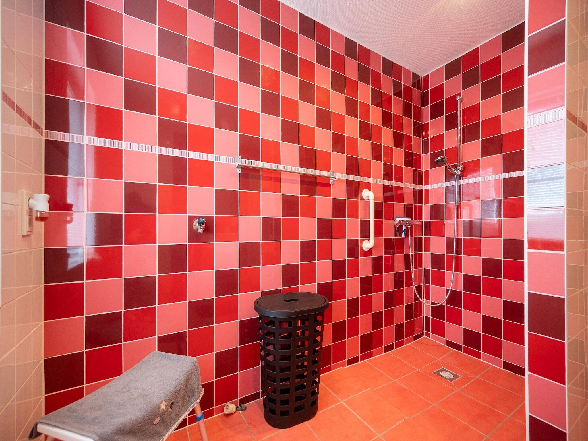 A bathroom with red and white checkered tiles, a shower, a towel rack, and a waste bin.