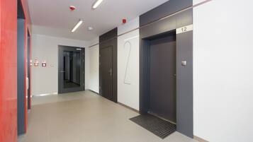 Un couloir moderne avec un mur d’accent rouge, une porte portant le numéro 12 et un détecteur d’incendie fixé au mur.