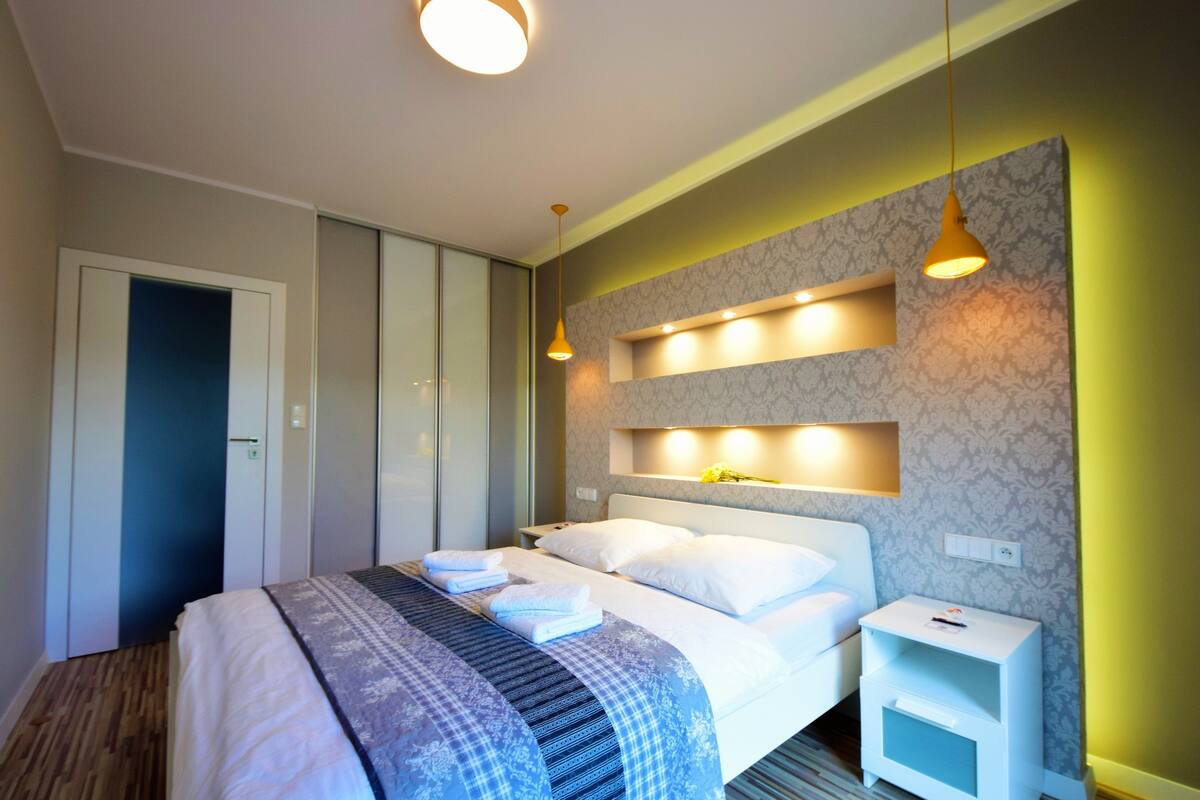 Ein modernes Hotelzimmer mit einem großen Bett, Nachttischen und integrierter Beleuchtung.