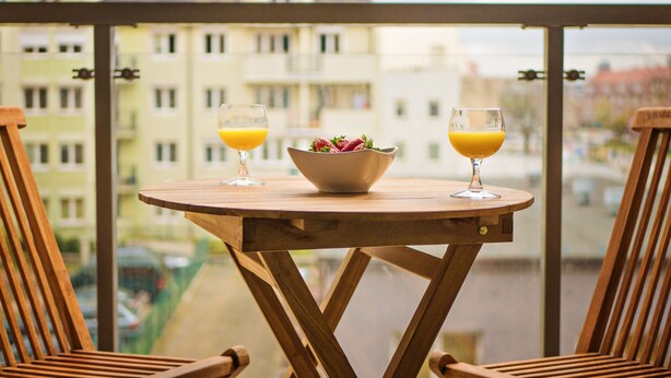Ett träbord med två glas apelsinjuice och en skål med frukt på en balkong med utsikt över staden.