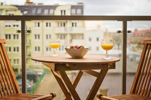 Una mesa de madera con dos vasos de zumo de naranja y un cuenco de fruta en un balcón con vistas a la ciudad.