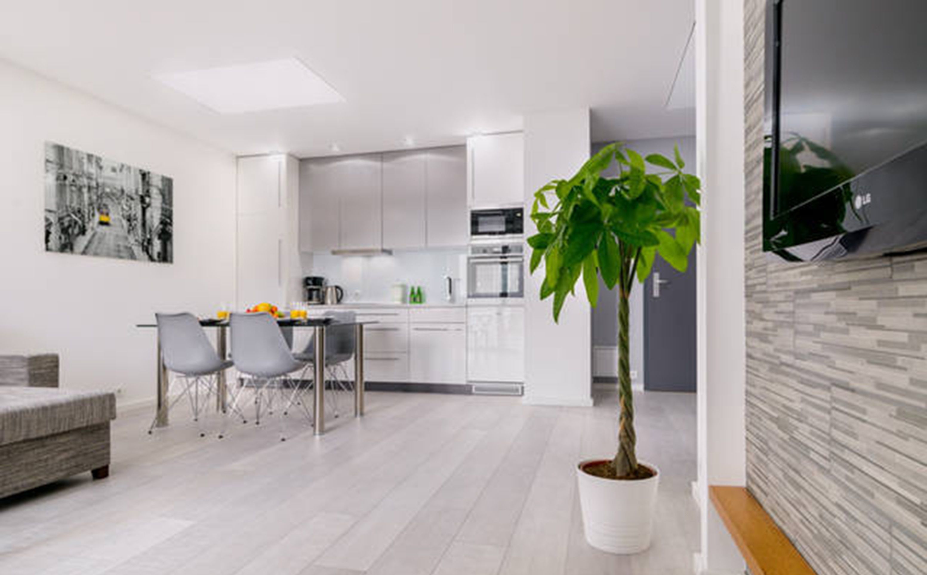 Een moderne keuken met witte kasten, een zithoek met een grijze bank en stoelen, en een potplant.