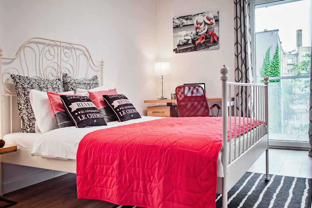 Ein ordentlich eingerichtetes Schlafzimmer mit Bett, Kissen, Nachttisch, Sessel und Aussicht ins Freie.