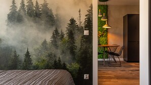 Ett sovrum med en väggmålning som föreställer en skog, en säng, en matplats med stolar och hängande lampor.