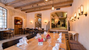 Een restaurant met een lange houten tafel gedekt voor een maaltijd, stenen muren en een open haard.