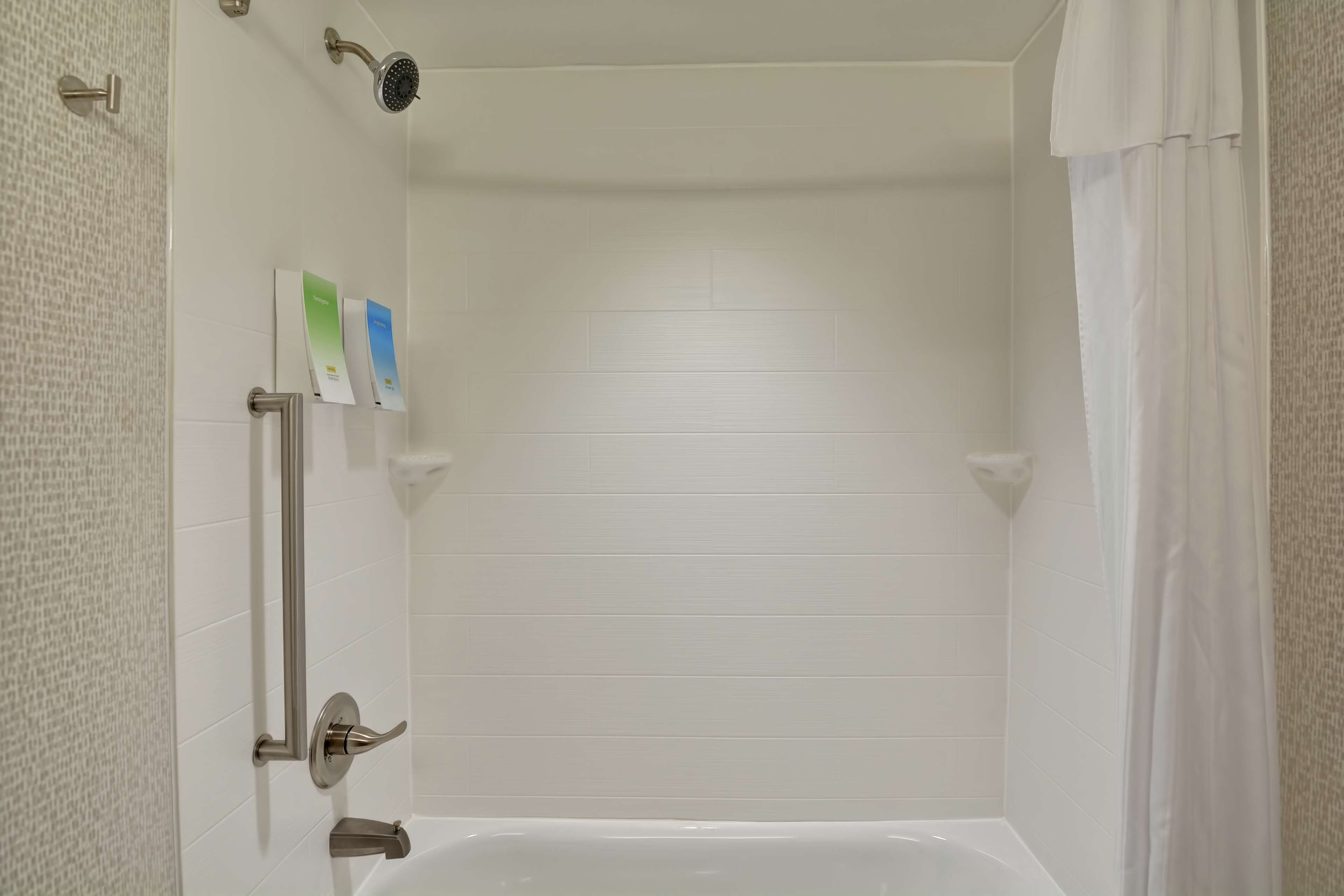 A bathroom with a white bathtub, a showerhead, and a handrail.