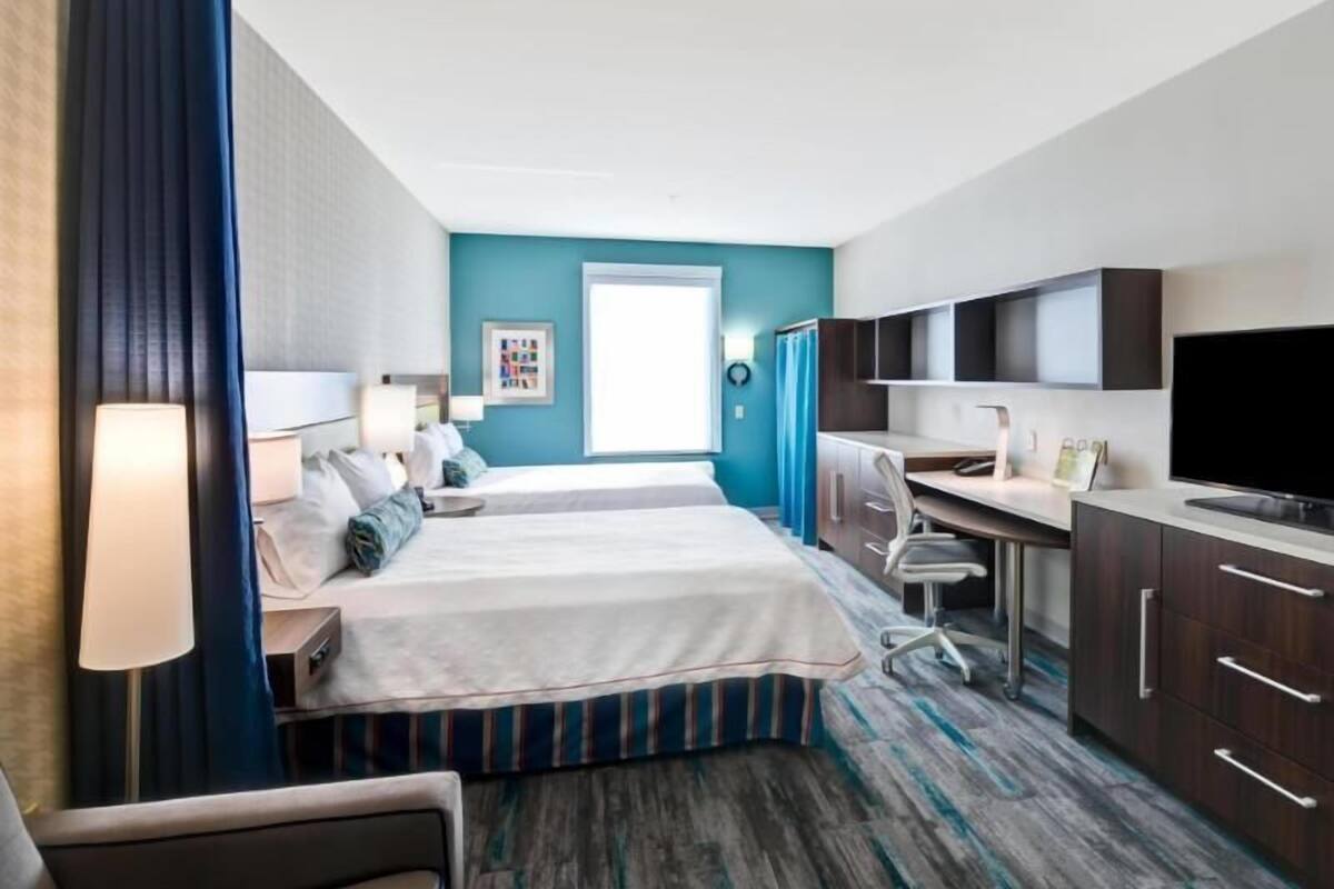 A hotel room with a bed, desk, chair, TV, and a window.