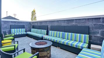 An outdoor seating area with wicker furniture and striped cushions, a stone fire pit, and a stone wall backdrop.