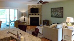 A living room with a fireplace, a ceiling fan, and a television mounted above it.