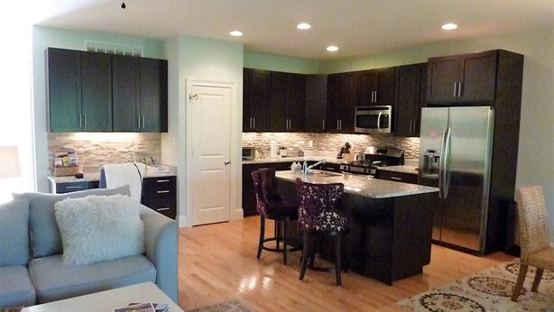 A modern kitchen with dark cabinets, a central island with bar stools, a refrigerator, and a microwave.