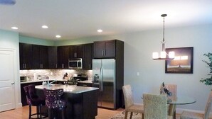 A modern kitchen with dark cabinets, a central island, and a dining area with a round table and chairs.