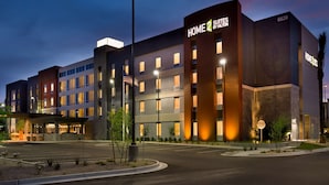 A modern hotel with a prominent "Home 2 Suites by Hilton" sign, multiple floors, and a well-lit entrance area.