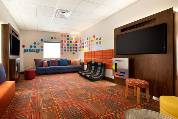 Un área de juegos con un sofá azul, decoraciones coloridas en la pared y un televisor grande.