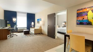 A hotel room with a desk, chair, bed, and a painting on the wall.
