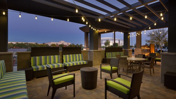 An outdoor seating area with wicker furniture and green cushions, under a pergola with string lights.