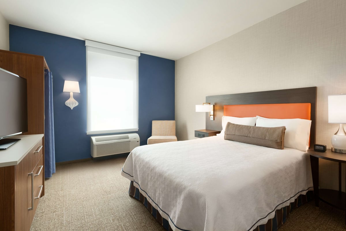 A hotel room with a large bed, a desk with a computer, a chair, and a window with curtains.