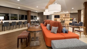 A modern hotel lobby with a seating area, a bar, and a kitchen in the background.
