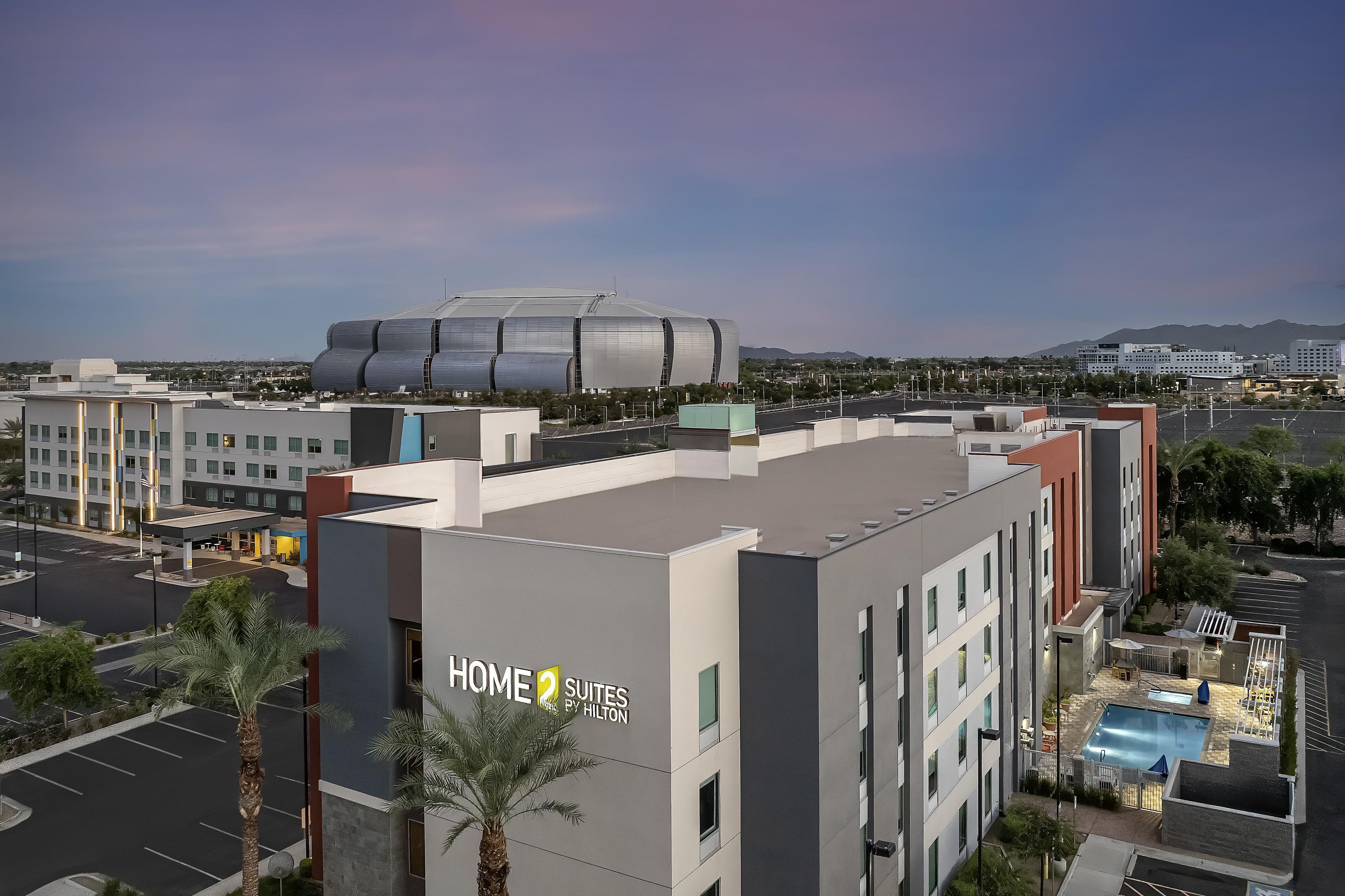 Un hotel con un letrero que dice 'HOME 2 SUITES BY HILTON' y una zona de piscina.