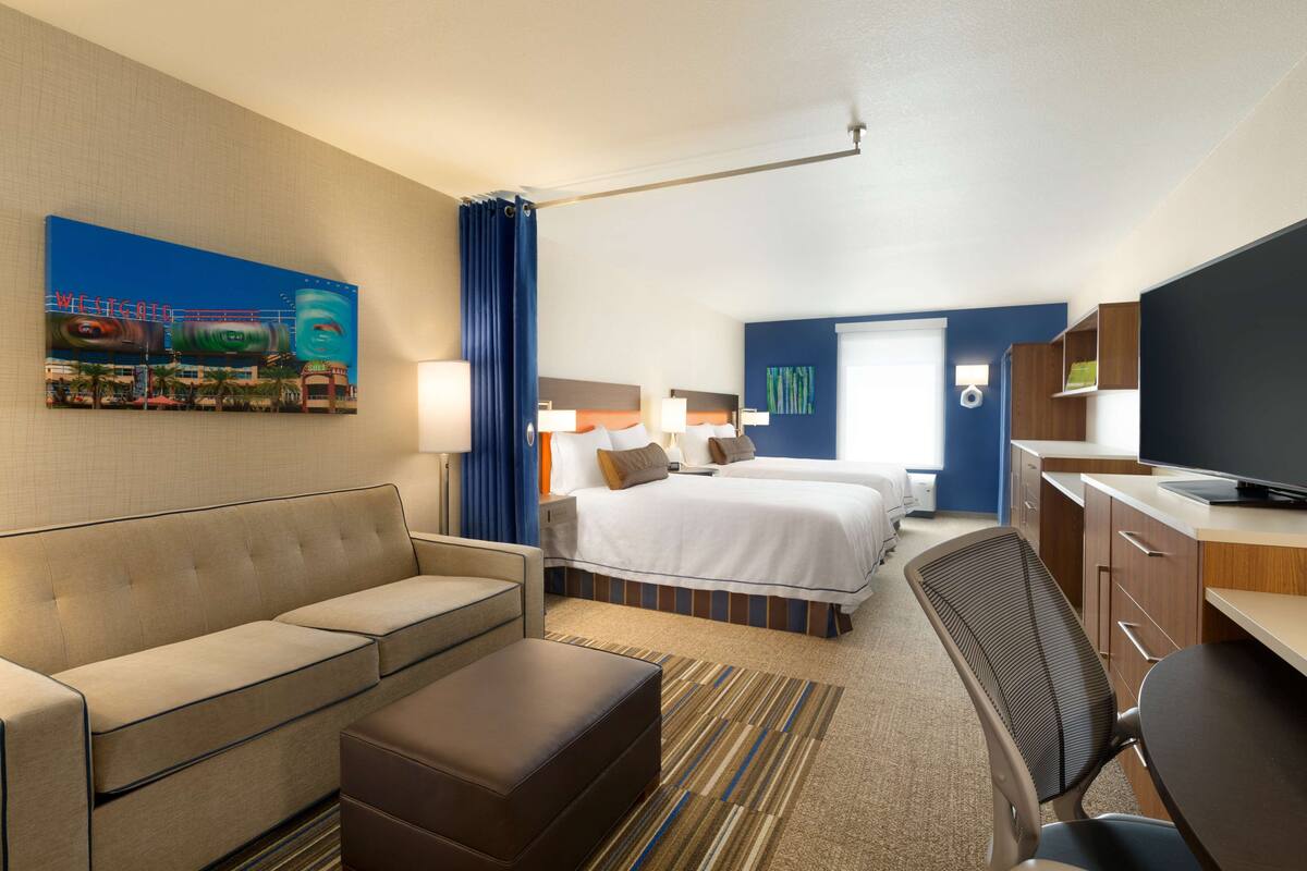 A hotel room with a bed, a sofa, a desk, and a television.