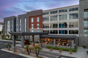 A modern hotel with a covered outdoor seating area and a parking lot.
