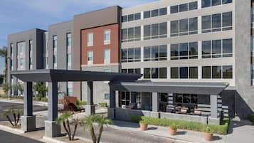 A modern building with multiple floors, a covered outdoor seating area, and a parking lot.