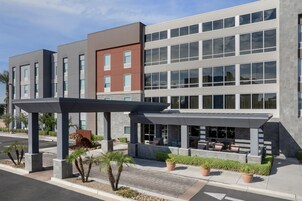 Un edificio moderno con varios pisos, una zona de estar exterior cubierta y un estacionamiento.