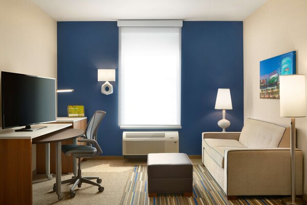 A hotel room with a desk, chair, sofa, and a TV.