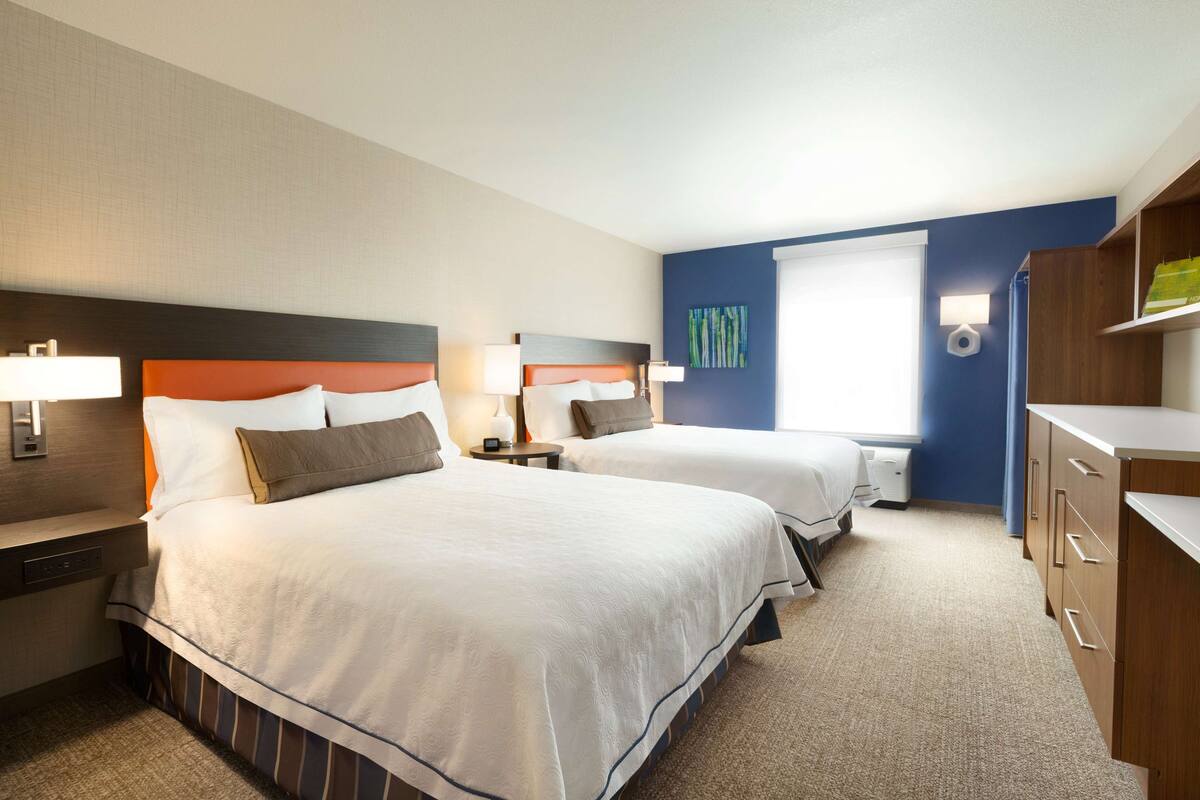 A hotel room with two beds, a desk, and a wardrobe.
