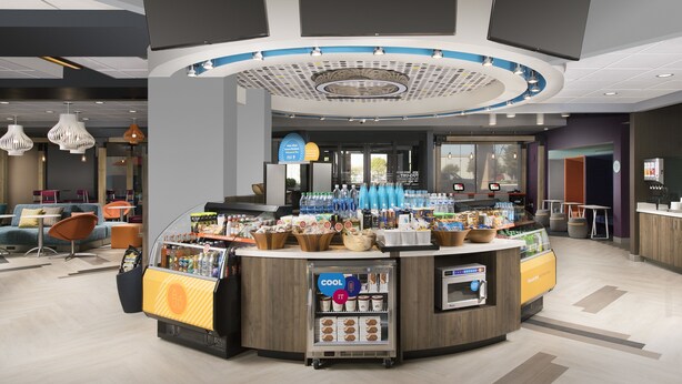 A modern cafe with a central counter, seating area, and a ceiling with recessed lighting. - Tru by Hilton Murfreesboro (Murfreesboro)