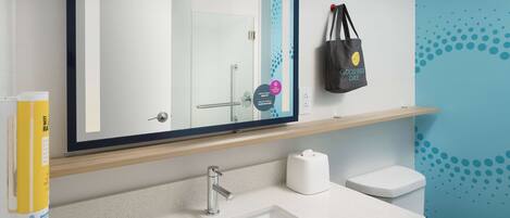 A modern bathroom with a large mirror, a sink, a toilet, and a towel dispenser.