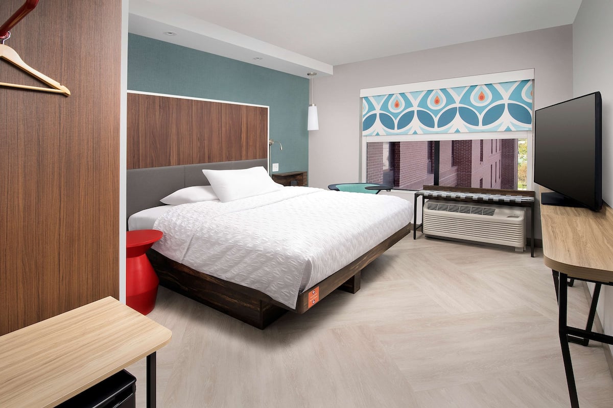 Habitació d'hotel moderna amb llit, televisió, escriptori i finestra amb persianes decoratives.