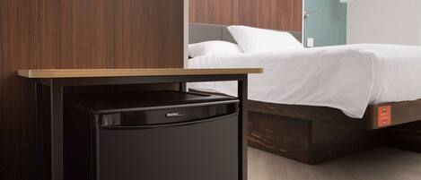 A compact room with a bed, a small black appliance, and a wooden table.