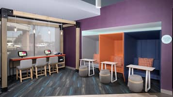 A modern office space with a glass wall, a desk with a computer, and seating areas with tables and chairs.