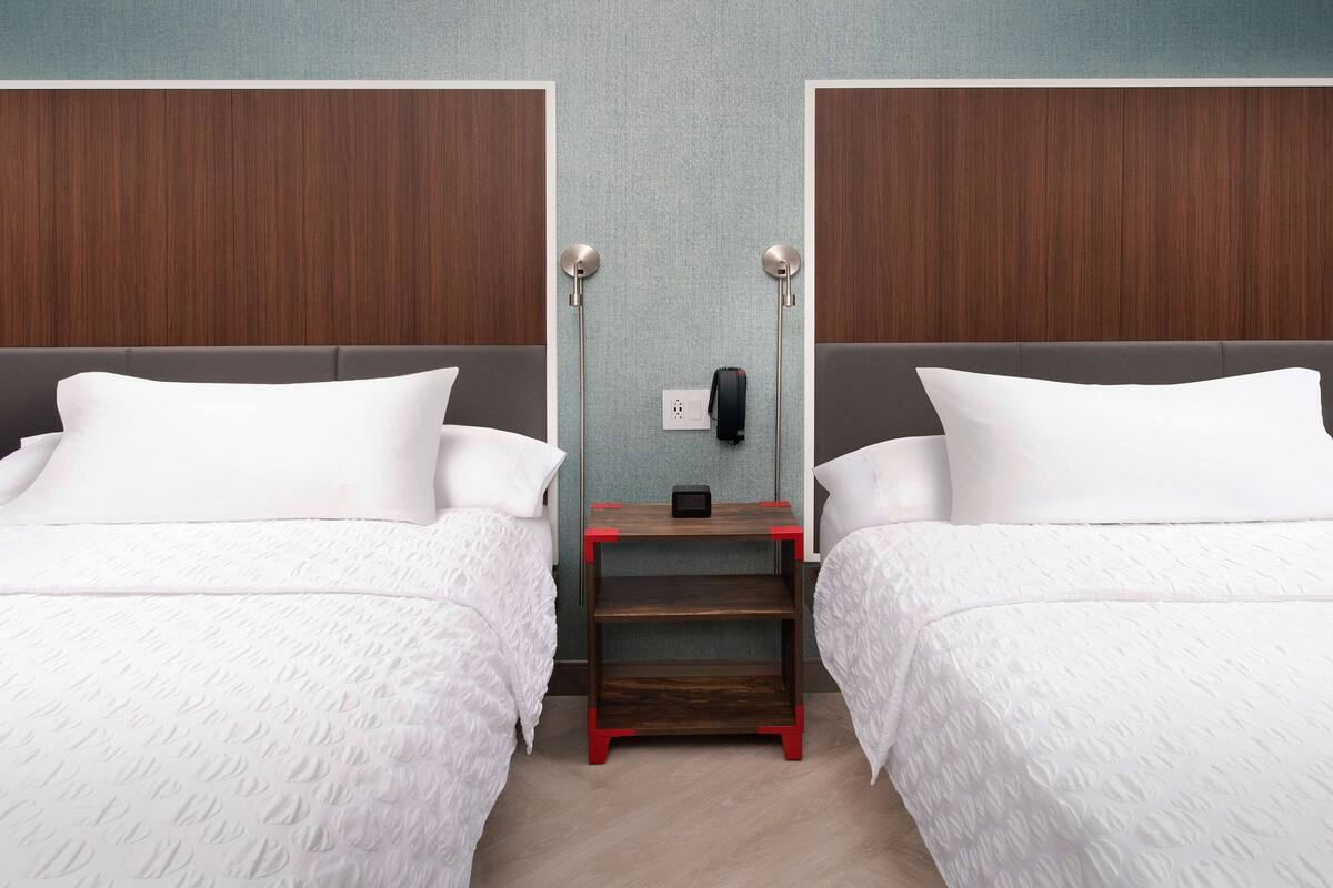 Habitació d'hotel amb dos llits, una tauleta de nit amb una làmpada i un telèfon fixat a la paret.