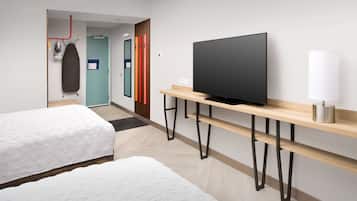 A hotel room with two beds, a TV on a wooden stand, and a bathroom visible through an open door.