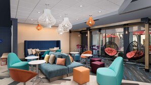 A modern lounge area with a blue sofa, orange and teal chairs, and hanging chairs with orange cushions. - Tru by Hilton Murfreesboro (Murfreesboro)
