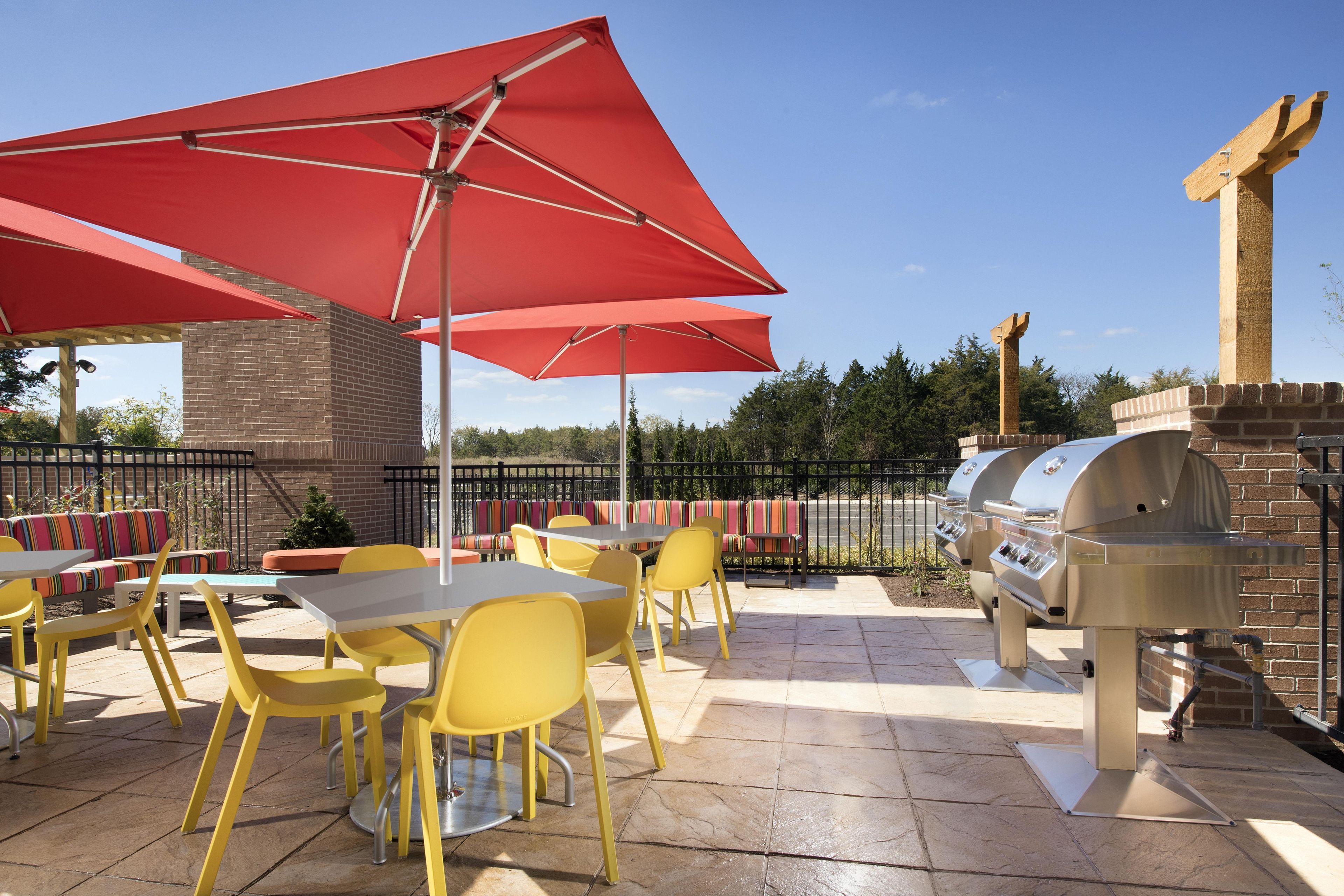 Une terrasse extérieure avec des chaises jaunes, des parasols rouges et un barbecue.