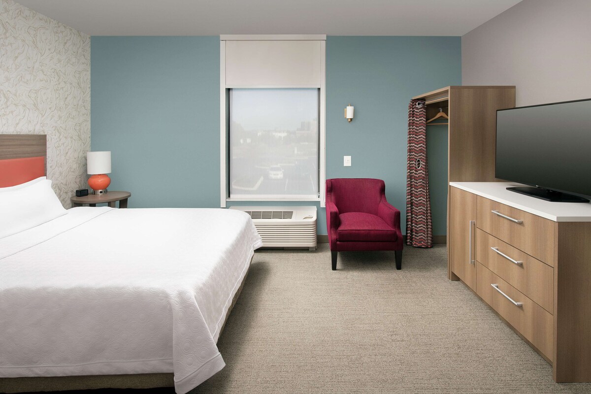 A hotel room with a bed, a red chair, a television, and a wardrobe.