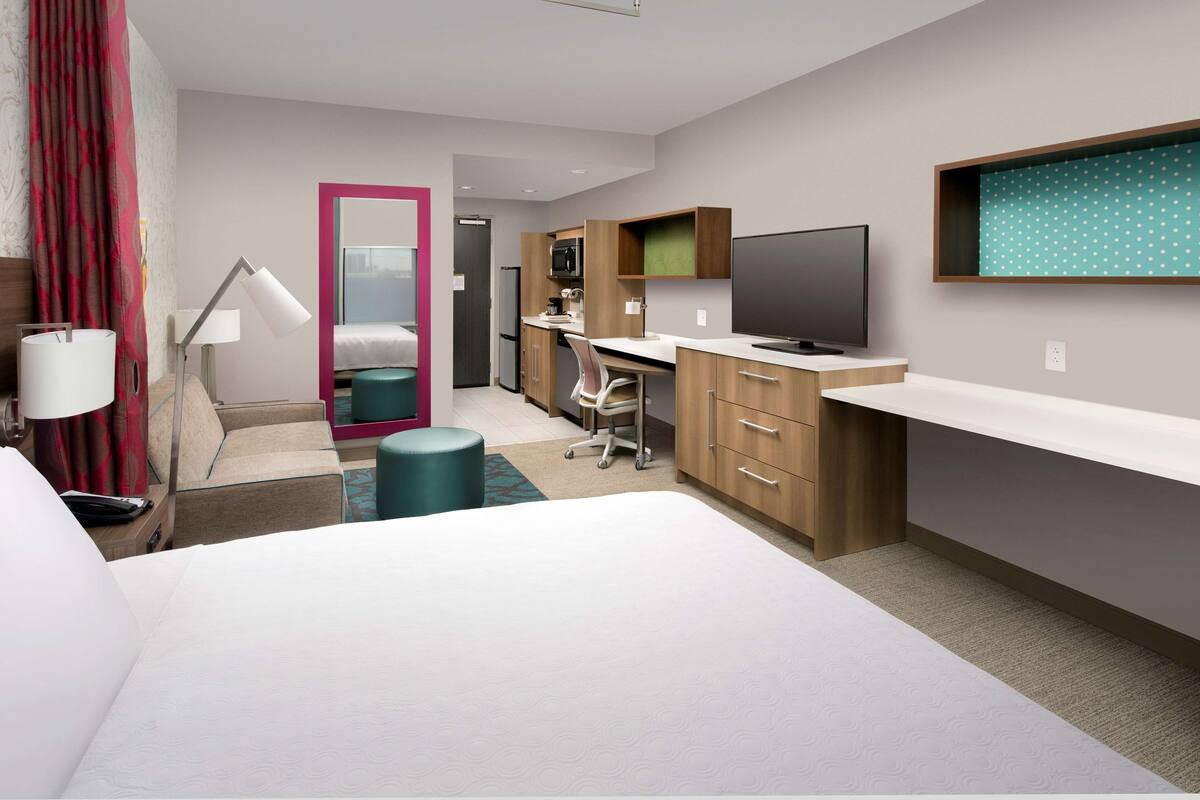 Habitació d'hotel moderna amb llit, escriptori, cadira, televisió i una cuineta petita.