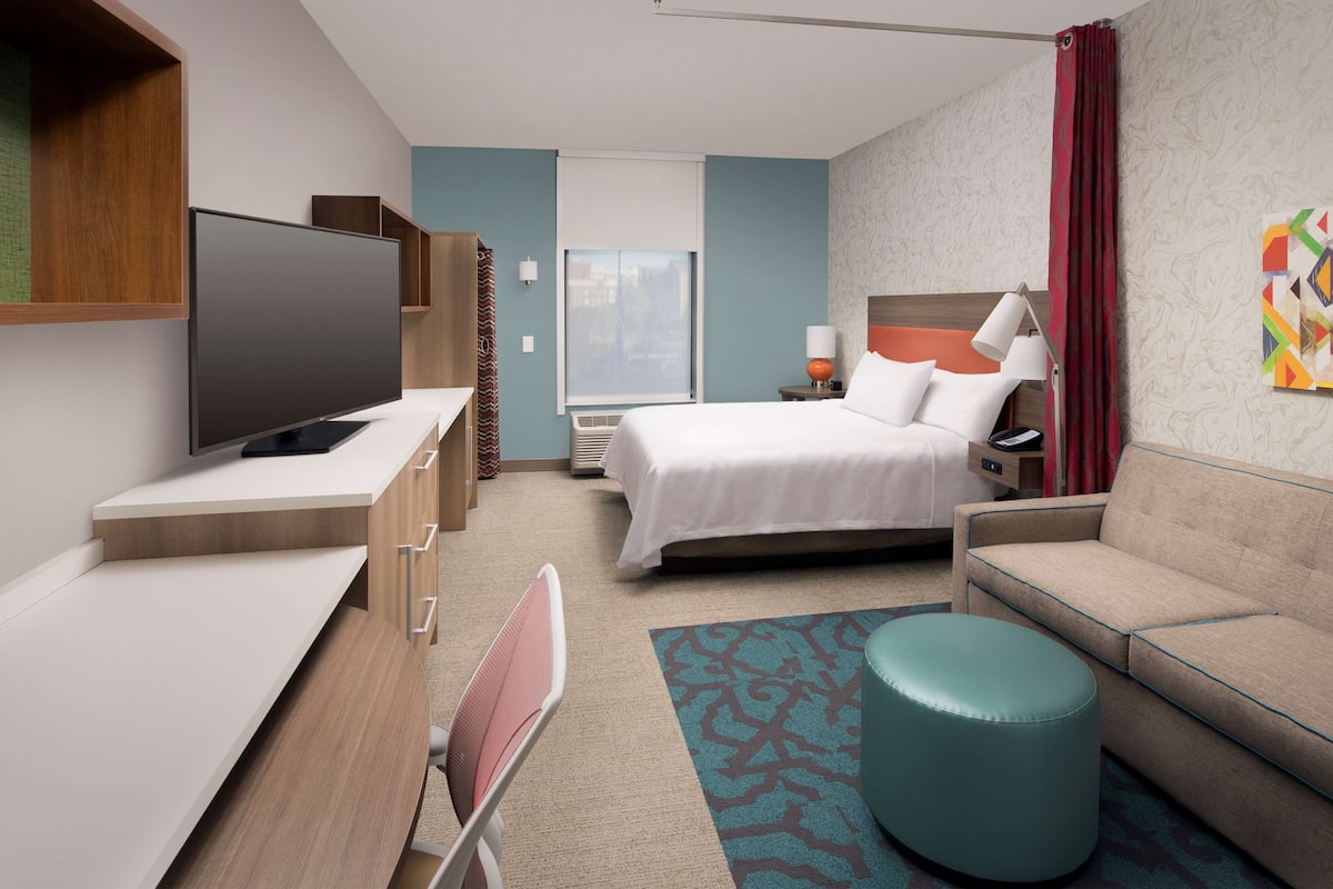 Habitació d'hotel moderna amb televisió de pantalla plana, llit, sofà, escriptori i cadira.