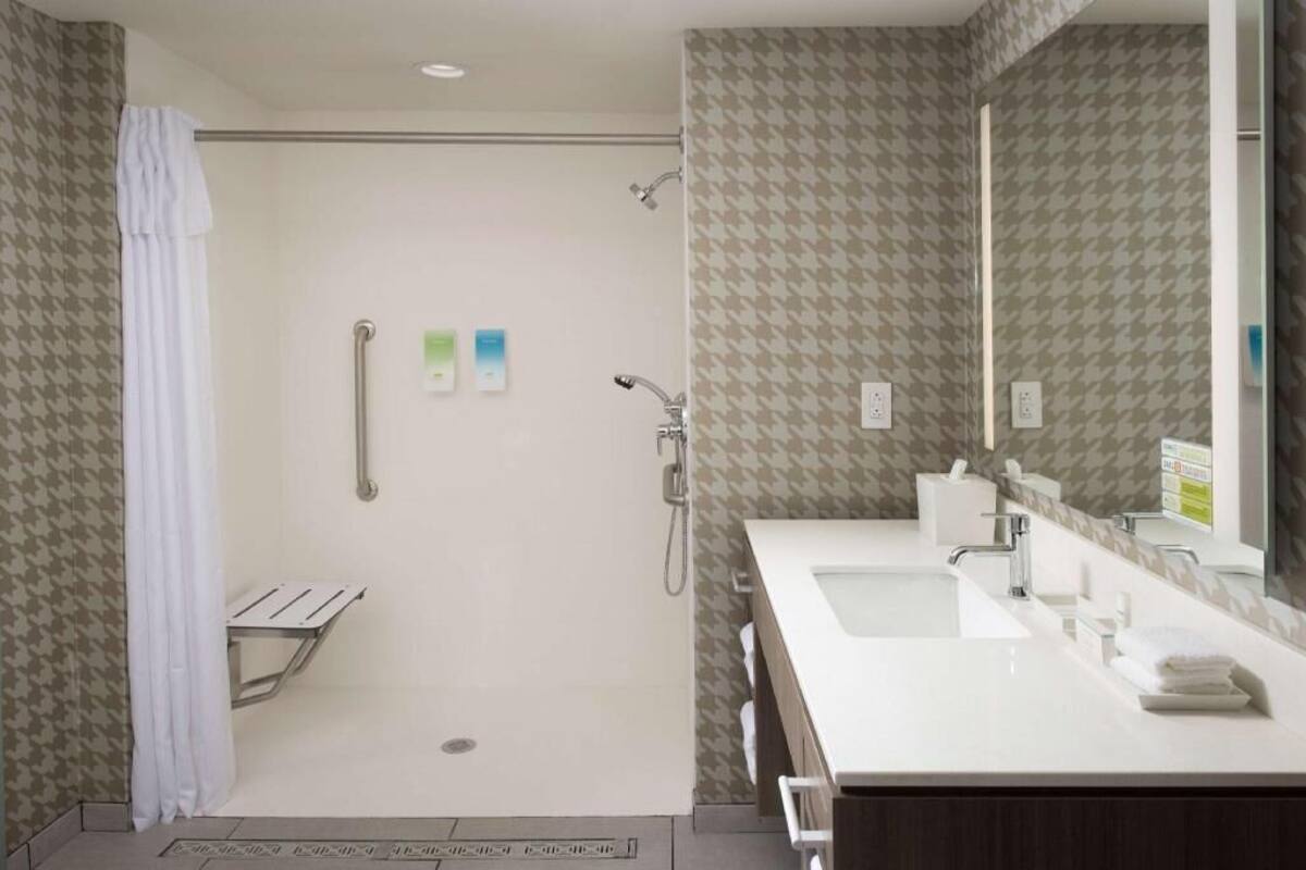 A bathroom with a shower, a sink, a mirror, and a towel rack.