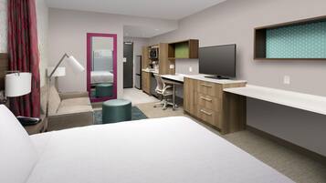 A hotel room with a bed, desk, chair, TV, and kitchenette.