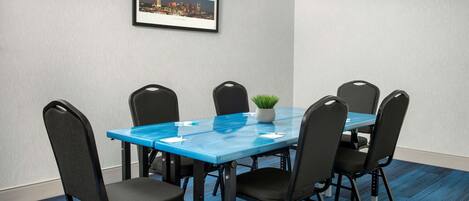 Een vergaderruimte met een blauwe tafel, zwarte stoelen en een lijst met een stadsgezicht op de muur.