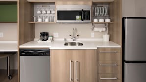 A compact kitchen with a built-in microwave, coffee maker, and dishwasher. - Home2 Suites by Hilton Murfreesboro (Murfreesboro)