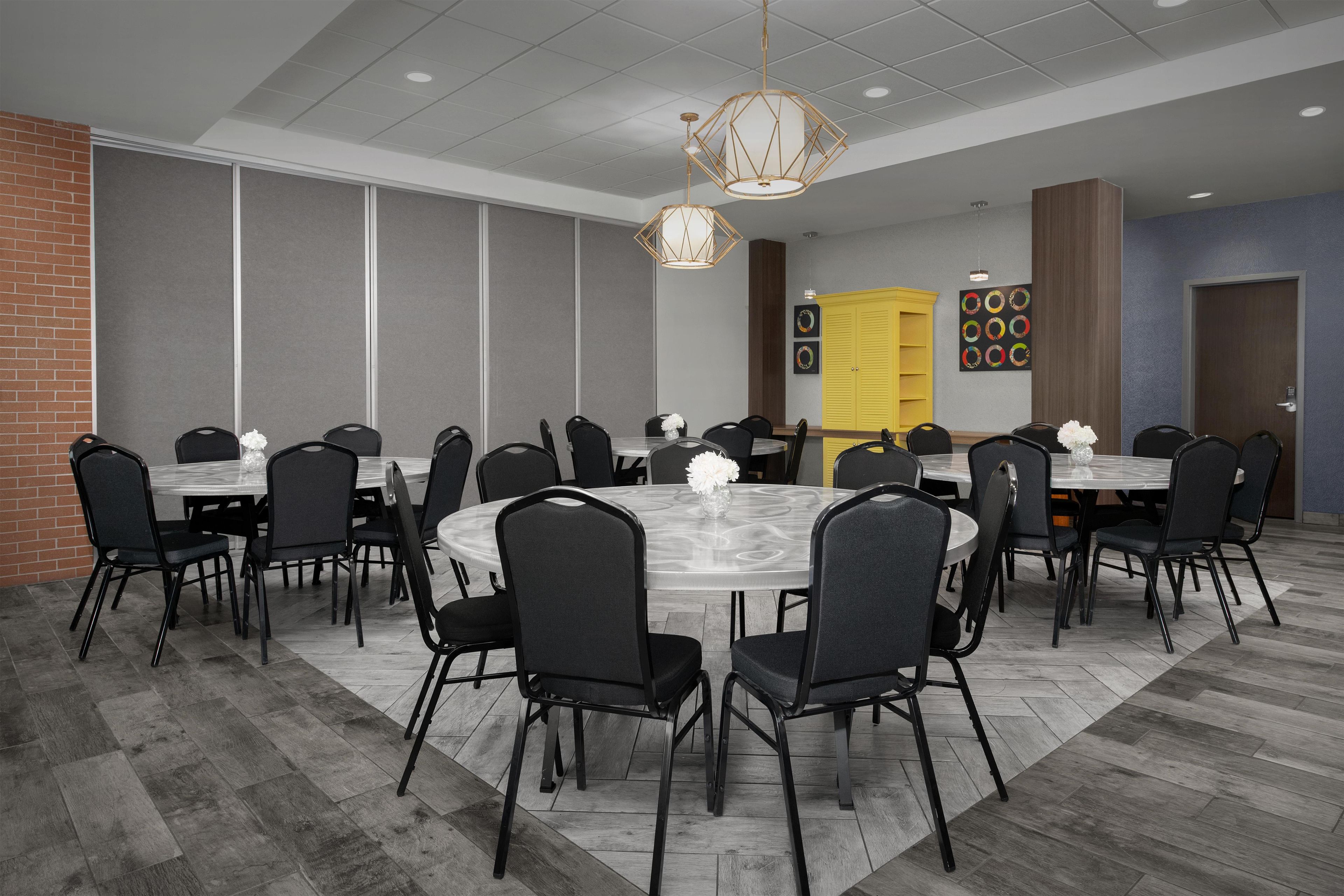 Un salón de conferencias con mesas y sillas redondas, una pared de ladrillo y un armario amarillo.